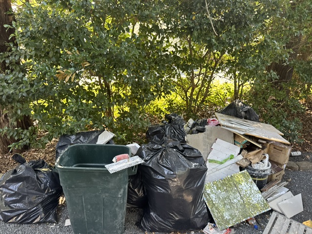 Before: multiple demo bags, tile, cardboard, and renovation waste piled in driveway area during Pinehurst renovation