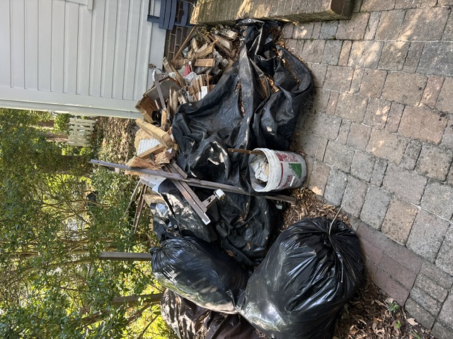 Before: renovation debris pile on back patio of historic Pinehurst Village home — lumber, demo bags, construction waste